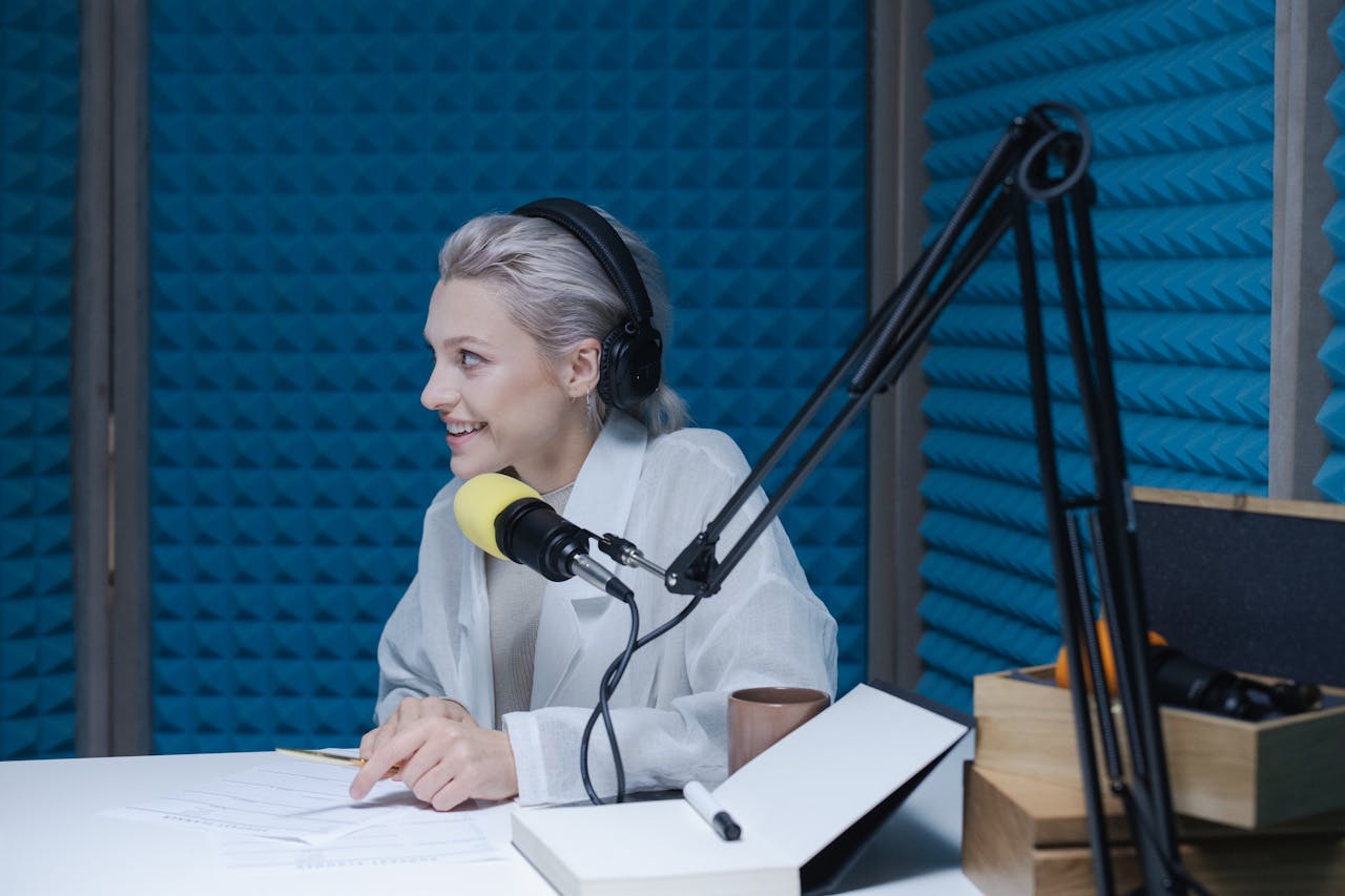 Woman wearing headphones recording a podcast in a soundproof studio with a microphone.